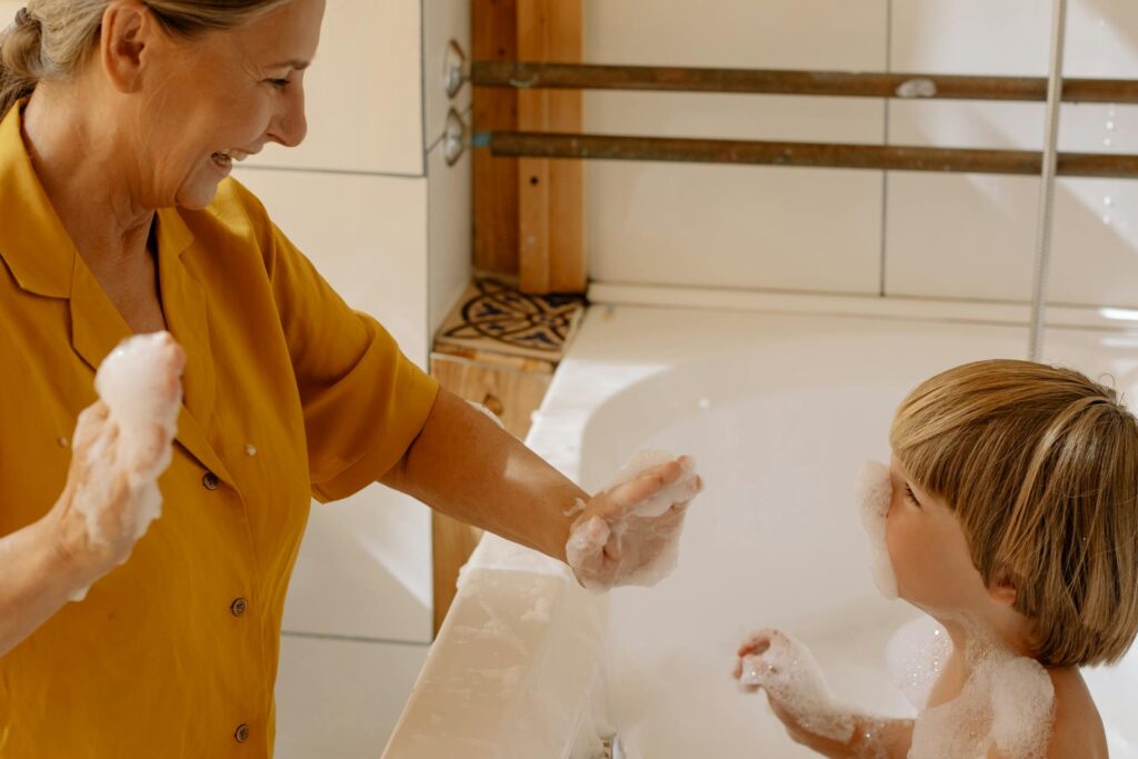 Eine Frau und ein Kind genießen gemeinsam ein Schaumbad im Badezimmer. Das Kind sitzt in der Badewanne und beide haben Spaß mit dem Schaum. Die modernen Badarmaturen im Hintergrund unterstreichen die gemütliche Atmosphäre.