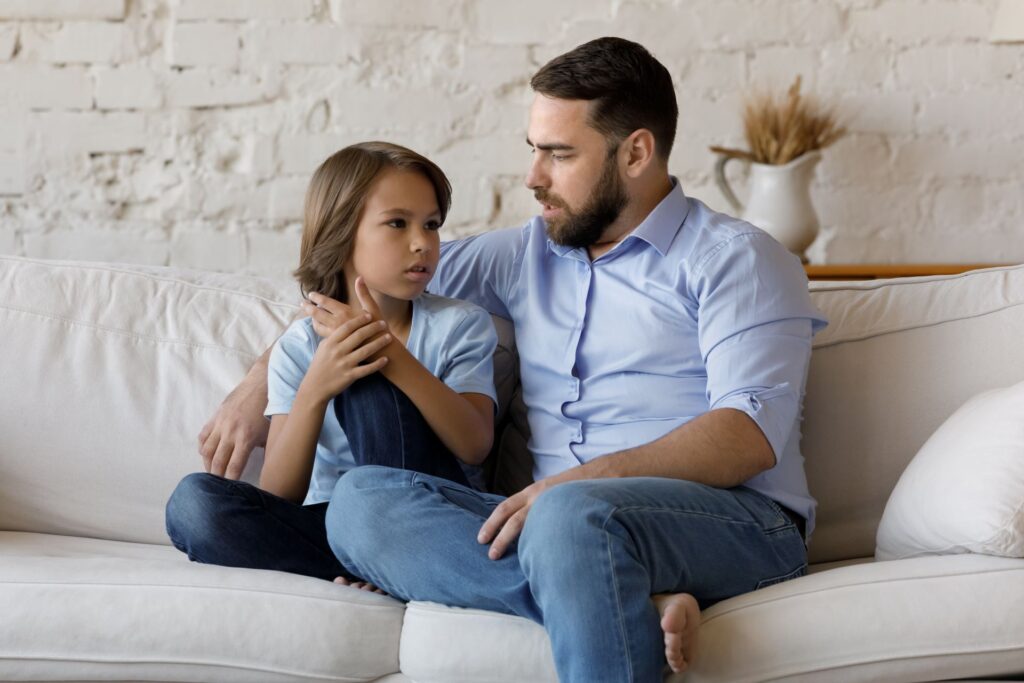 Vater hört seinem kleinen Sohn im Teenageralter zu, der zu Hause auf dem Sofa sitzt und mit ihm spricht. Der Junge teilt seine Probleme, fragt Pappa um Rat. Kommunikation, Fürsorge und Vertrauens Konzept