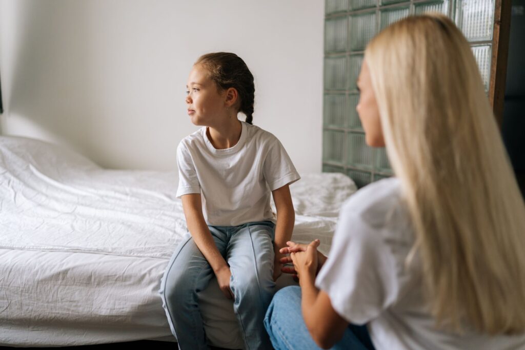 Eine Mutter spricht ernsthaft mit ihrer jungen Tochter, während sie auf dem Bett sitzt. Dieses Bild symbolisiert familiäre Gespräche und die Bedeutung von Unterstützung im Kontext des Familienrechts in Würzburg.