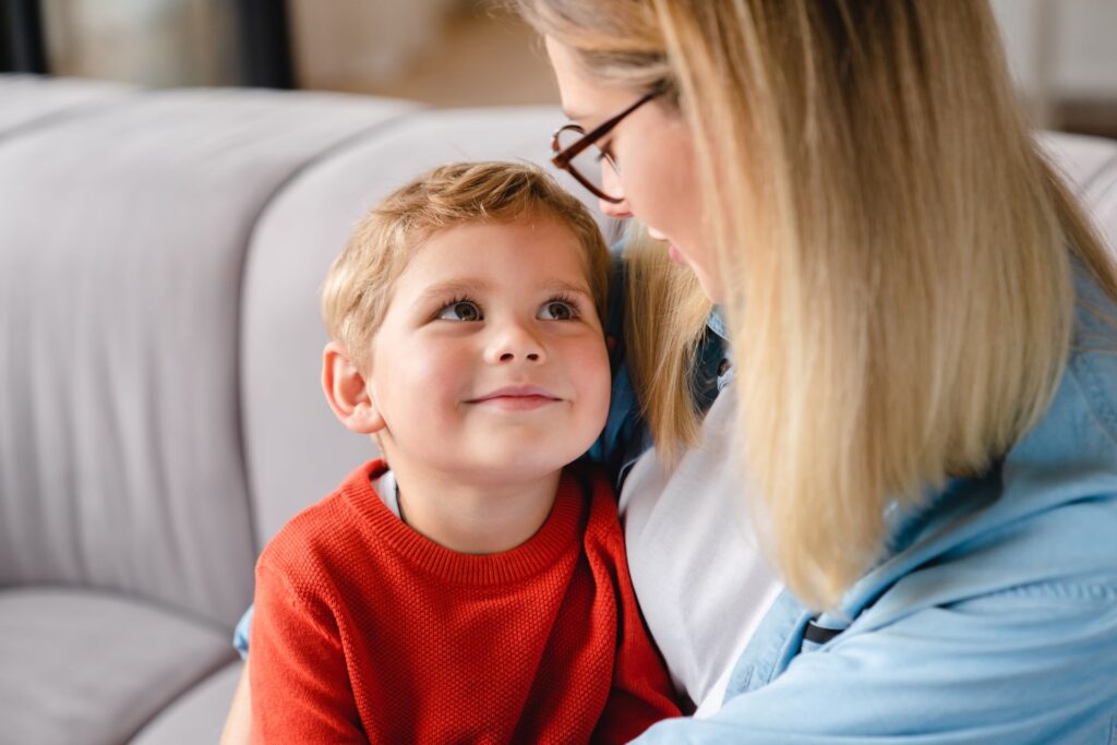 Eine Mutter sitzt mit ihrem jungen, lächelnden Sohn auf dem Sofa. Diese Szene steht für die enge Bindung und die emotionale Unterstützung innerhalb der Familie, relevant für das Familienrecht in Würzburg.