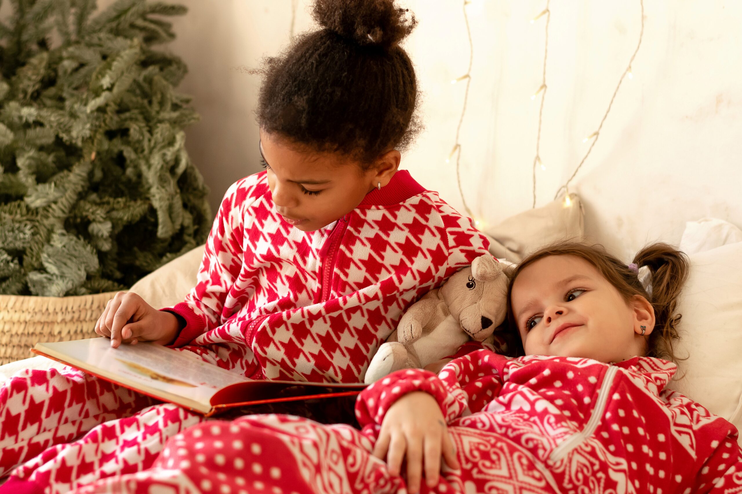 Zwei Schwestern lesen zusammen ein Buch und tragen weihnachtliche Pyjamas